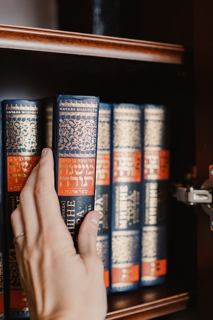 Close-up of a hand reaching for a Torah book on a bookshelf, symbolizing Jewish culture.